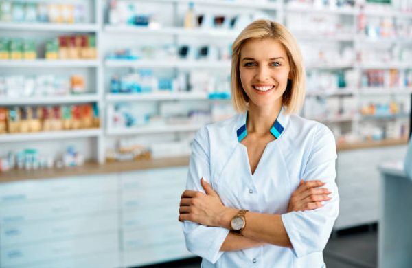 farmacista Happy pharmacist standing with her arms crossed in a pharmacy and looking at camera.